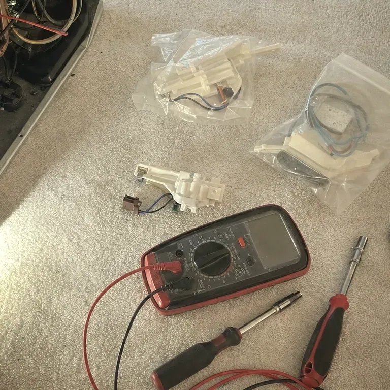 Red multimeter, a screwdriver and small bagged parts on a beige carpet.